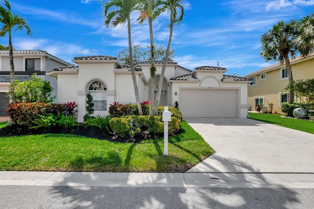 mediterranean / spanish-style home with a front yard, stucco siding, concrete driveway, an attached garage, and a tile roof