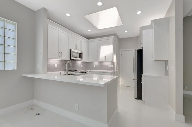 kitchen featuring a skylight, appliances with stainless steel finishes, a sink, light countertops, and a peninsula