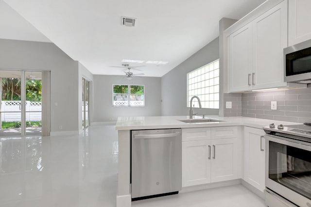 kitchen with a sink, a peninsula, tasteful backsplash, a ceiling fan, and appliances with stainless steel finishes