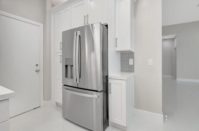 kitchen with backsplash, light countertops, baseboards, stainless steel fridge, and white cabinetry