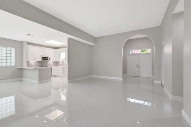 unfurnished living room with a sink, baseboards, arched walkways, and finished concrete floors