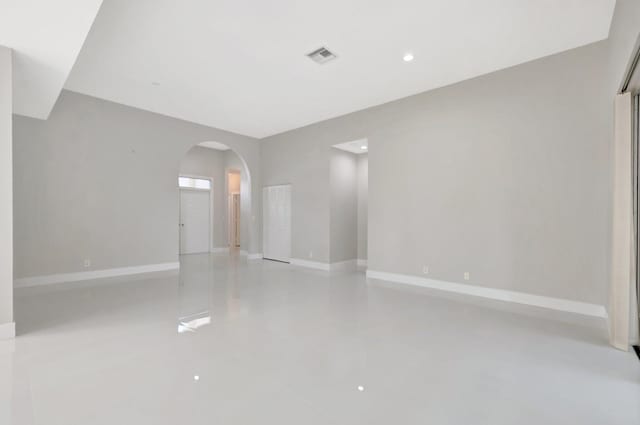 spare room with arched walkways, baseboards, visible vents, and finished concrete flooring