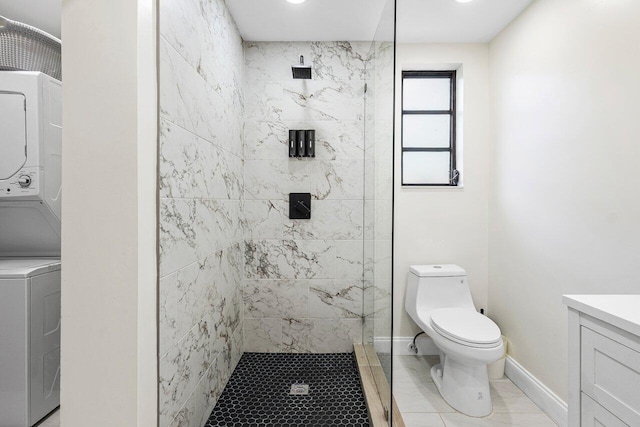 bathroom featuring a tile shower, stacked washer and dryer, vanity, toilet, and baseboards