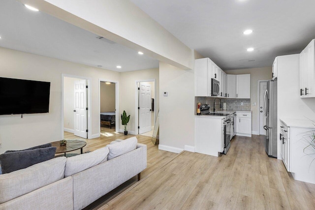 kitchen featuring open floor plan, light countertops, decorative backsplash, light wood finished floors, and appliances with stainless steel finishes