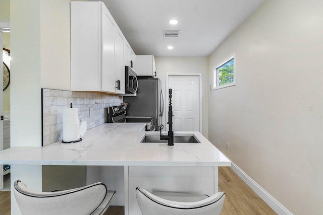 kitchen with a peninsula, white cabinetry, light wood-style floors, decorative backsplash, and stainless steel appliances