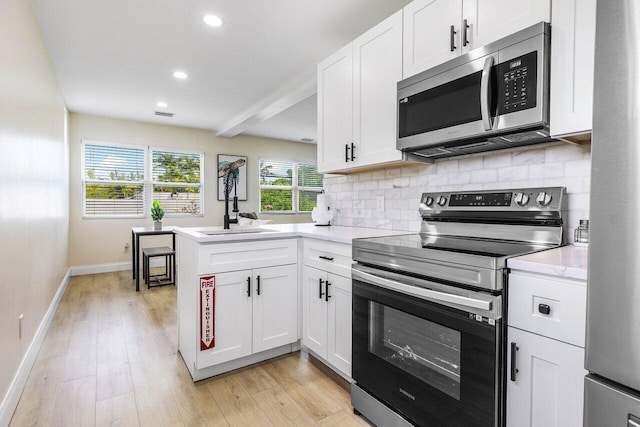 kitchen featuring white cabinets, light countertops, appliances with stainless steel finishes, a peninsula, and decorative backsplash