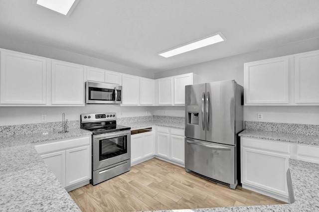 698 SW Mchole Ave, Port Saint Lucie, FL 34953 - kitchen with white cabinets, appliances with stainless steel finishes, a skylight, and light wood-type flooring