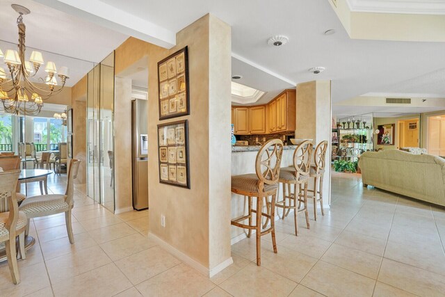 interior space with an inviting chandelier, light tile patterned floors, ornamental molding, stainless steel fridge, and a raised ceiling