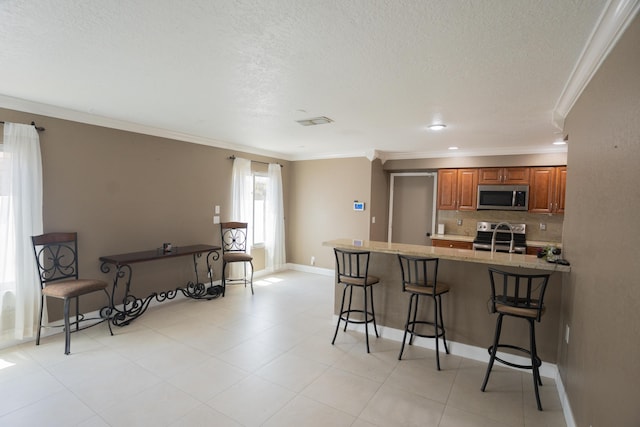 5740 Teakwood Rd, Lake Worth, FL 33467 - kitchen with crown molding, a kitchen bar, a peninsula, appliances with stainless steel finishes, and brown cabinets