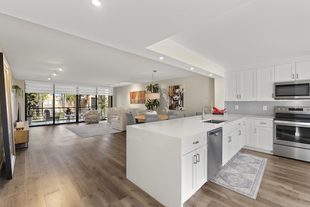 kitchen featuring a peninsula, a sink, light countertops, stainless steel appliances, and open floor plan