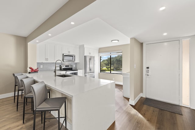 kitchen featuring white cabinetry, recessed lighting, wood finished floors, a sink, and stainless steel appliances