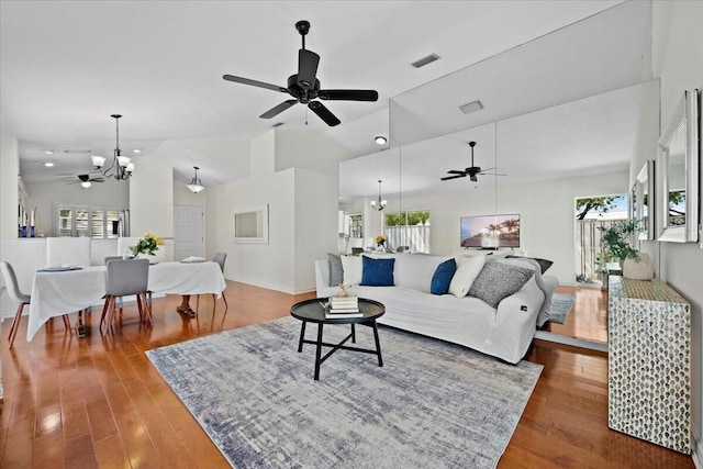 living area with ceiling fan with notable chandelier, wood finished floors, and a healthy amount of sunlight