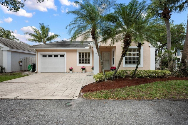 view of front facade with stucco siding, decorative driveway, an attached garage, a tiled roof, and fence