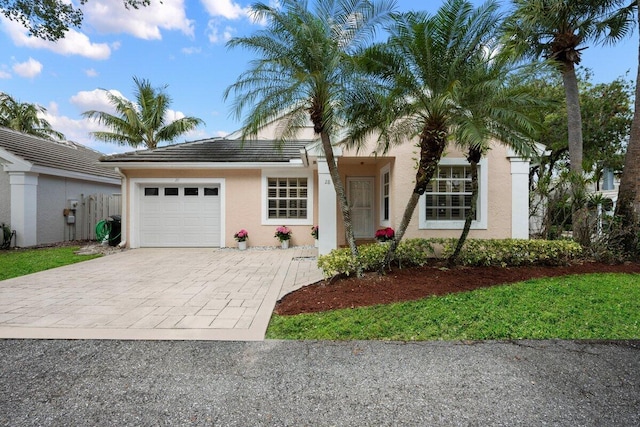 view of front of house featuring a tiled roof, stucco siding, decorative driveway, fence, and a garage