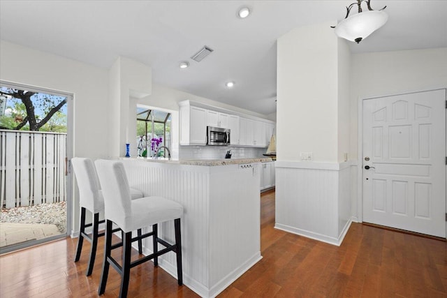 kitchen with a kitchen breakfast bar, dark wood-type flooring, white cabinetry, visible vents, and stainless steel microwave