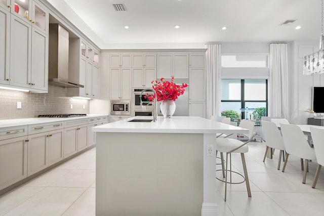 kitchen with stainless steel appliances, light tile patterned floors, wall chimney exhaust hood, and a kitchen bar