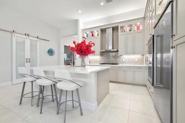 kitchen with wall chimney range hood, light countertops, backsplash, a breakfast bar area, and gas stovetop