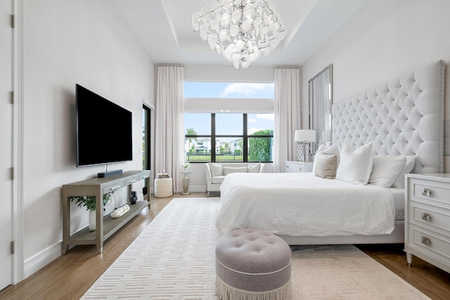 bedroom with a chandelier, wood finished floors, a tray ceiling, and baseboards