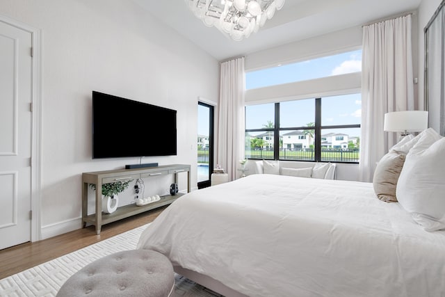 bedroom featuring wood finished floors, high vaulted ceiling, a notable chandelier, and baseboards