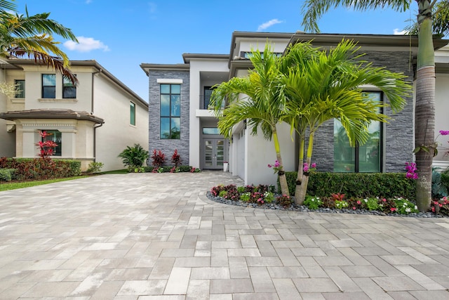 view of front facade featuring french doors, stone siding, decorative driveway, and stucco siding