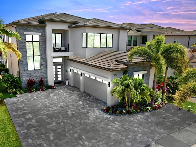 view of front of house featuring a balcony, a tiled roof, stone siding, and stucco siding