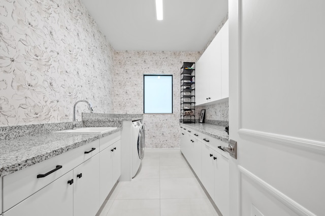 clothes washing area featuring wallpapered walls, light tile patterned flooring, independent washer and dryer, cabinet space, and a sink
