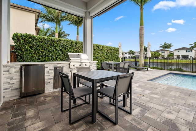 view of patio / terrace featuring area for grilling, a water view, fence, exterior kitchen, and outdoor dining space