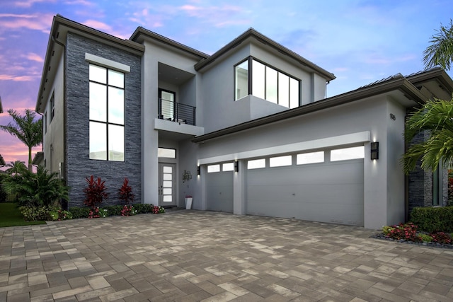 contemporary house with stucco siding, stone siding, decorative driveway, and a balcony