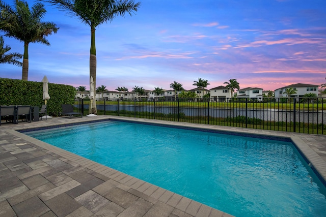 pool at dusk featuring a water view, a patio, fence, a fenced in pool, and a residential view