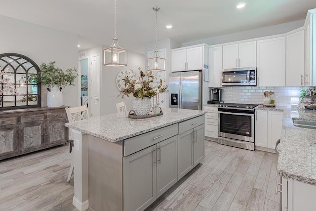 348 SE Courances Dr, Port Saint Lucie, FL 34984 - kitchen featuring stainless steel appliances, light wood-type flooring, backsplash, a kitchen island, and light stone countertops