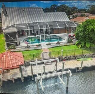 dock area featuring an outdoor pool, a yard, a lanai, and a water view