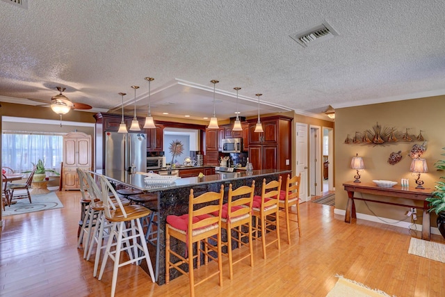 108 NE Carlisle Ln, Port Saint Lucie, FL 34952 - kitchen featuring visible vents, ornamental molding, stainless steel appliances, light wood-style flooring, and a breakfast bar area