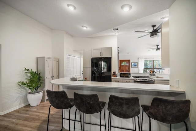 18292 126th Ter N, Jupiter, FL 33478 - kitchen featuring black fridge with ice dispenser, stainless steel range with electric cooktop, wood finished floors, and a breakfast bar