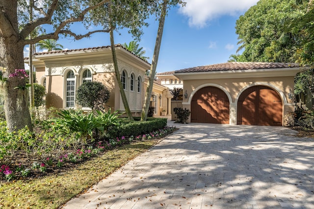 mediterranean / spanish-style home with driveway, stucco siding, an attached garage, and a tile roof