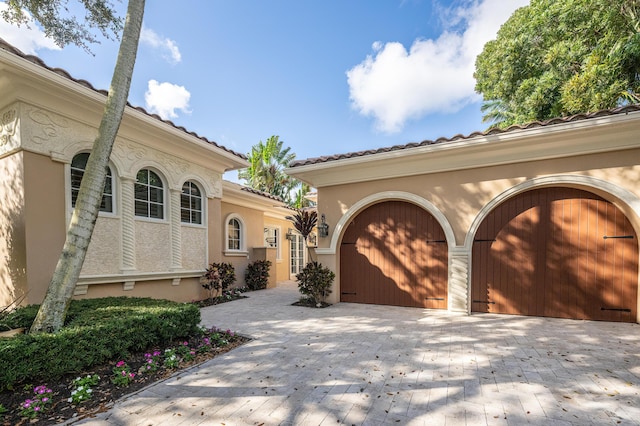 exterior space with a garage, stucco siding, decorative driveway, and a tile roof