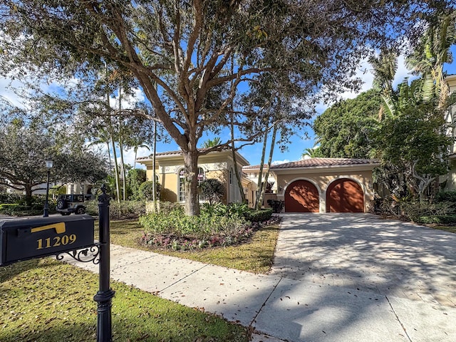mediterranean / spanish-style home featuring a tile roof, stucco siding, a garage, and concrete driveway