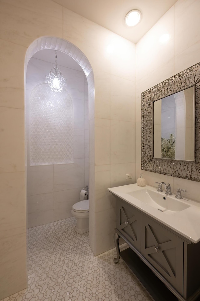 bathroom featuring toilet, a chandelier, vanity, and tile walls