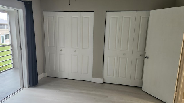 unfurnished bedroom featuring baseboards, light wood-type flooring, and two closets