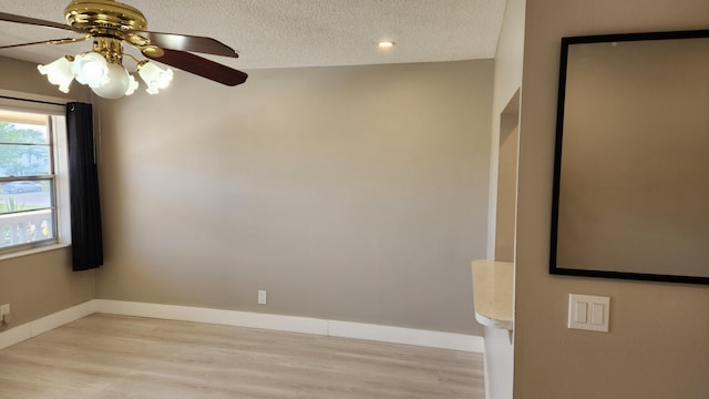 empty room featuring baseboards, light wood-type flooring, a ceiling fan, and a textured ceiling