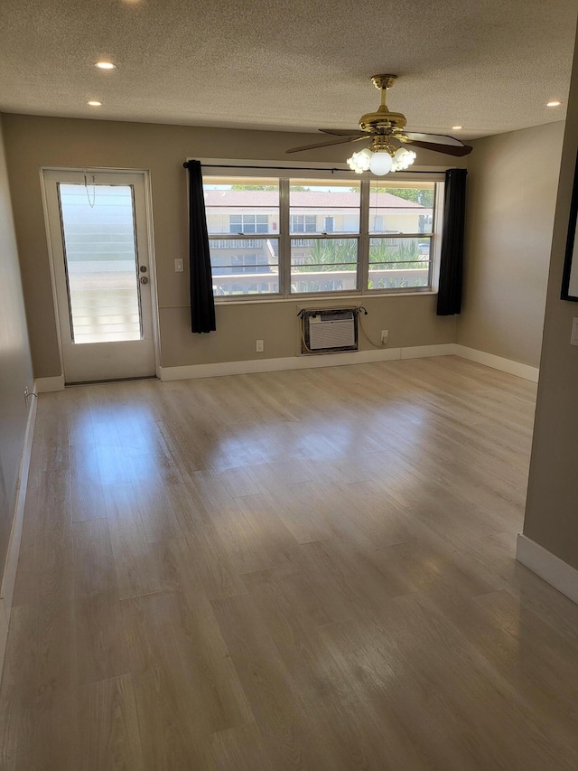 interior space featuring wood finished floors, a ceiling fan, baseboards, a wall mounted AC, and a textured ceiling