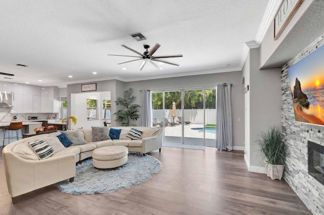 living room with crown molding, ceiling fan, wood finished floors, recessed lighting, and a stone fireplace