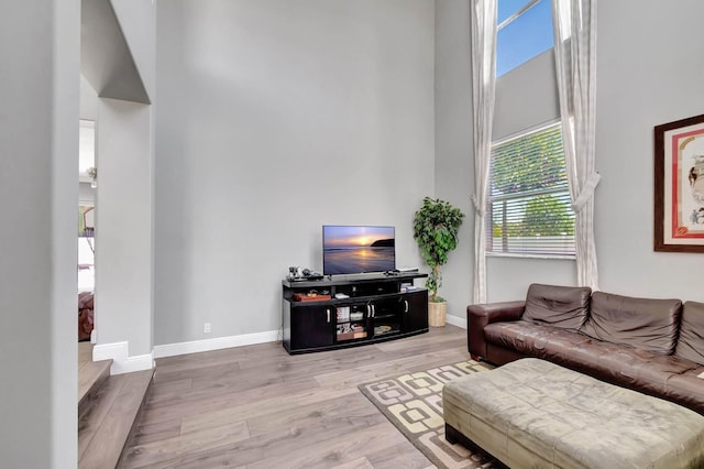 living room featuring a towering ceiling, wood finished floors, and baseboards