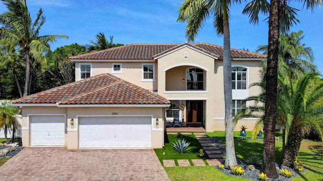mediterranean / spanish-style house with stucco siding, a tiled roof, and decorative driveway