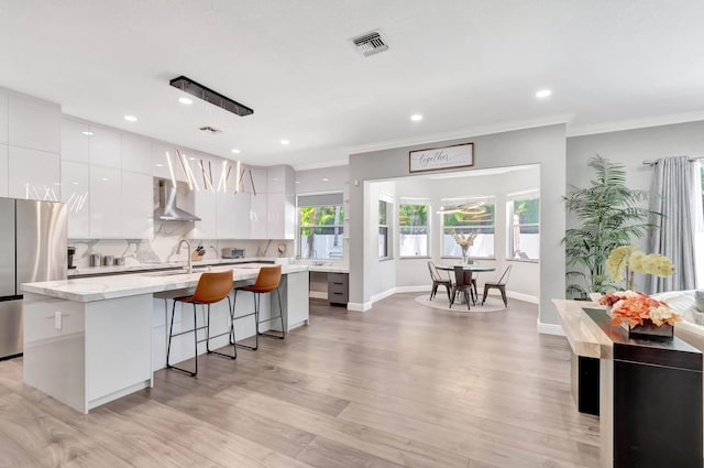 kitchen with modern cabinets, wall chimney exhaust hood, freestanding refrigerator, white cabinetry, and crown molding