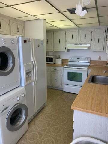 1905 NW 18th St Unit 101, Delray Beach, FL 33445 - kitchen featuring white appliances, under cabinet range hood, stacked washer / dryer, a sink, and light countertops