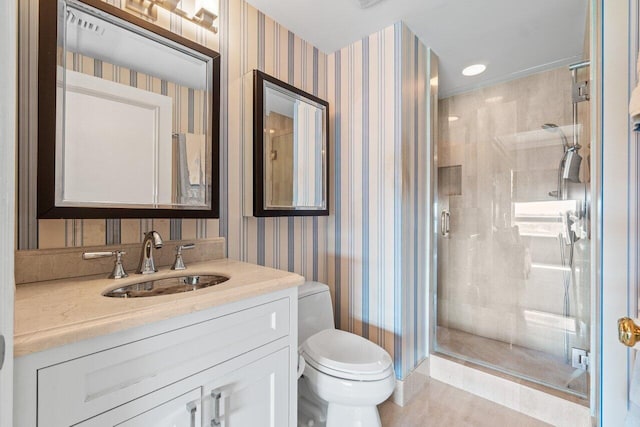 bathroom featuring a shower stall, vanity, wallpapered walls, and toilet