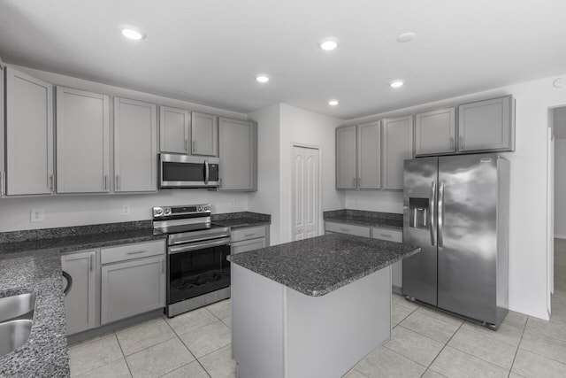 kitchen with dark stone countertops, gray cabinets, light tile patterned floors, a kitchen island, and stainless steel appliances