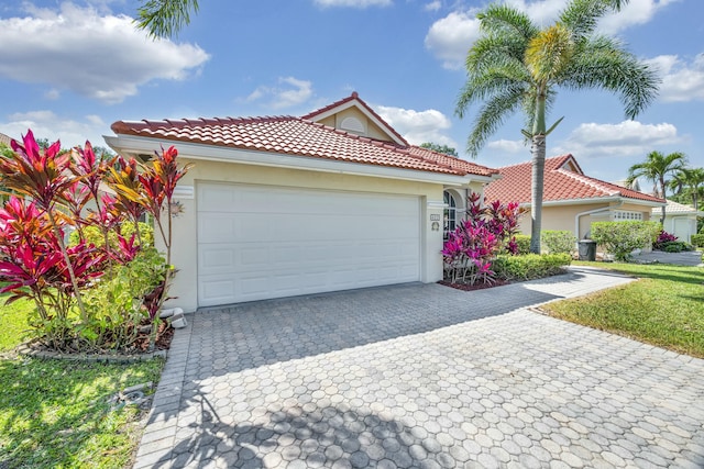 mediterranean / spanish-style home featuring a front lawn, stucco siding, a tile roof, decorative driveway, and a garage