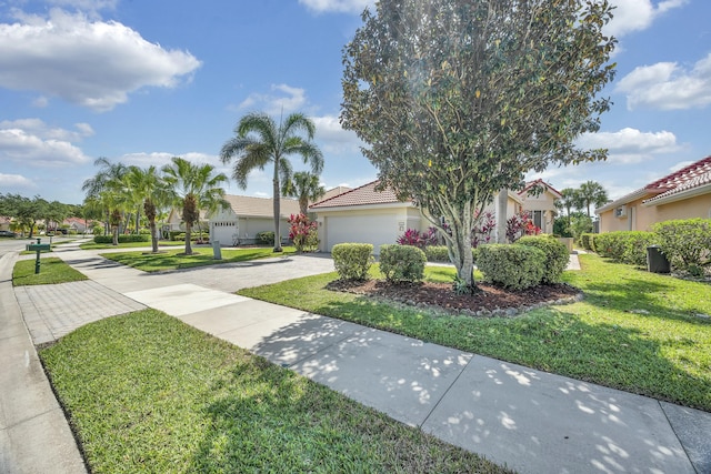 mediterranean / spanish home featuring a tile roof, decorative driveway, a front lawn, an attached garage, and stucco siding
