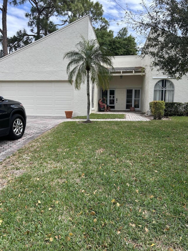view of front of house with an attached garage, driveway, a front yard, and stucco siding